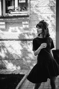 Beautiful young woman in dress standing by building