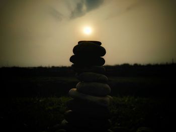 Stack of stones on field against sky during sunset