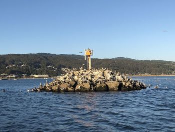 Lighthouse on rock by sea against clear blue sky