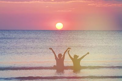 Silhouette people in sea against sky during sunset