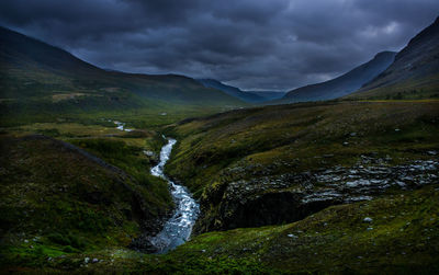 Scenic view of waterfall and mountains against cloudy sky