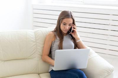 Young woman using phone while sitting on sofa