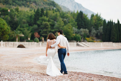 Rear view of couple standing on shore against trees