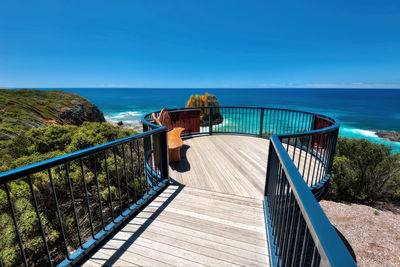 Footbridge over sea against clear blue sky