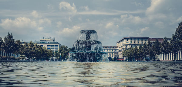 Fountain in city against cloudy sky