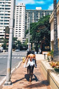 Rear view of woman carrying surfboard on street