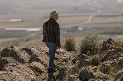 Rear view of adult man with cowboy hat standing on top of hill