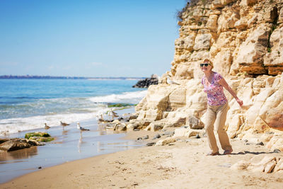 Elderly woman in sunglasses feeds seagulls on the beach