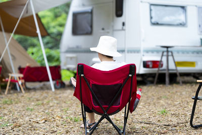Rear view of woman wearing hat sitting on chair against motor home