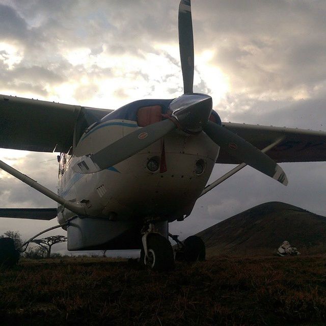 transportation, mode of transport, sky, air vehicle, airplane, cloud - sky, field, landscape, cloudy, cloud, aircraft wing, rural scene, flying, travel, sunset, outdoors, public transportation, part of, land vehicle, wind turbine