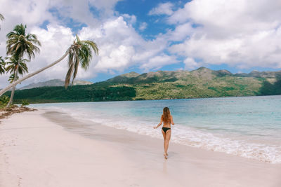 Rear view of woman standing on beach against sky