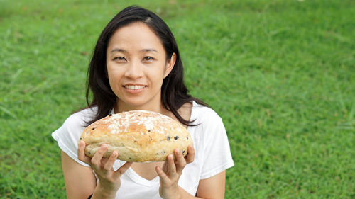 Portrait of smiling woman holding bread on grass