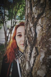 Portrait of a beautiful young woman standing by tree trunk