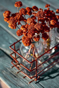 Rustic still life of dried brown flowers in glass jars inside vintage wire rack on wood tble