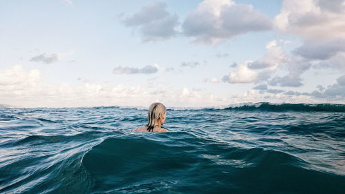 Rear view of blonde woman swimming in sea against cloudy sky