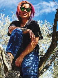 Young woman wearing sunglasses sitting on tree