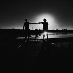 Silhouette people standing on railing against sky during sunset