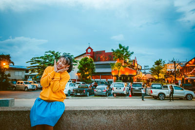 Smiling young woman with eyes closed gesturing while sitting on footpath