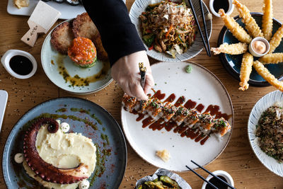 Hand picking a piece of sushi from a table filled with various delicious asian dishes