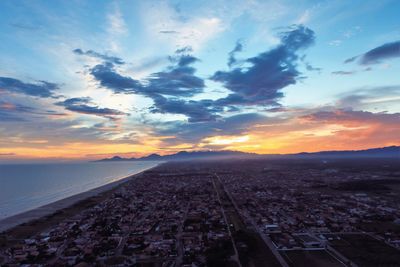 Aerial view of city by sea against sky during sunset