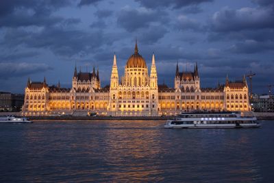 Parliament building by river against cloudy sky with boat in foreground