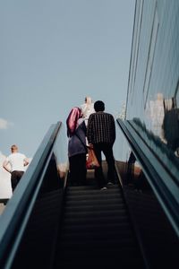 Low angle view of people on escalator against sky