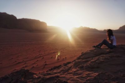 Man sitting on rock against sky during sunset