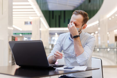 Frustrated businessman wearing mask sitting at mall