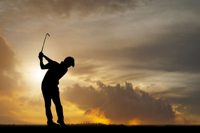 Silhouette man playing golf on field against sky during sunset