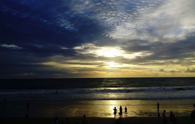 Silhouette people on beach against sky during sunset