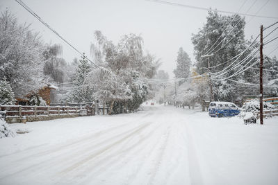 Snow covered road amidst trees against sky