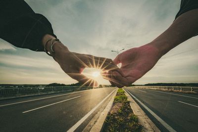 Man holding umbrella on road against sky during sunset