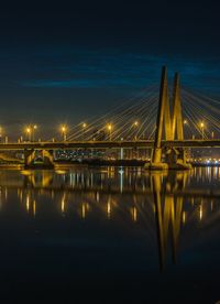 Illuminated bridge over river against sky at night