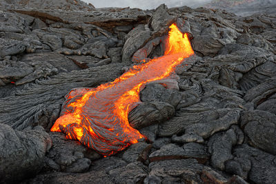 Hot magma of an active lava flow emerges from a rock fissure, glowing lava makes the air flicker