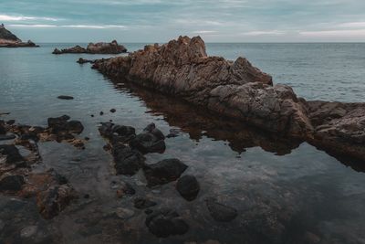 Rocks on shore by sea against sky