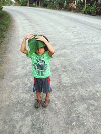Boy holding leaf on head while standing on road