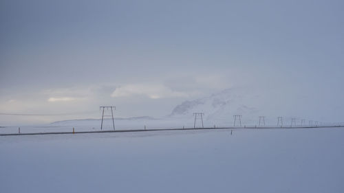 Snow covered electricity pylon against sky