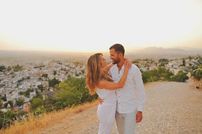 Romantic young couple standing on cobbled road against sky during sunset