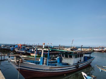 Boats moored at harbor against clear blue sky