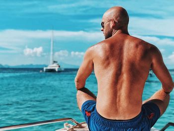 Rear view of shirtless man sitting at beach