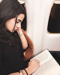 Woman reading book while sitting in airplane
