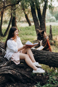 Young woman sitting on tree trunk against plants