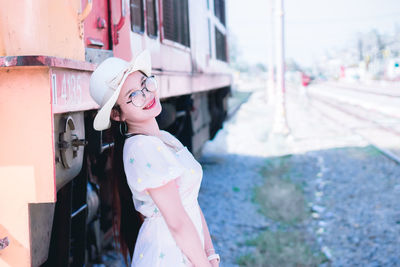 Portrait of smiling woman standing by locomotive by railroad track