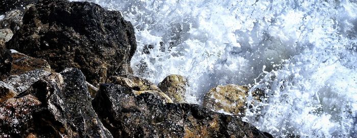 Waves splashing on rock formation against sky