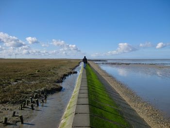 Rear view of person on footpath by sea against sky