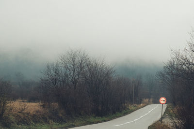 Road by bare trees against sky