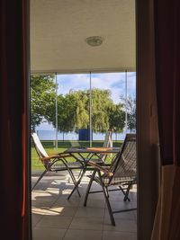 Chairs and table by swimming pool against trees seen through window