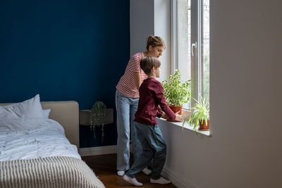 Rear view of woman using digital tablet while sitting on bed at home