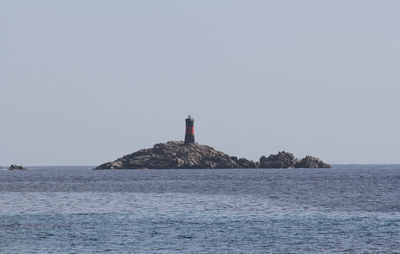 Lighthouse by sea against clear sky