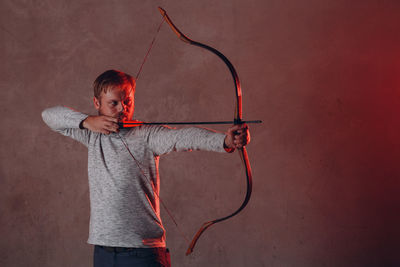 Man holding bow against wall